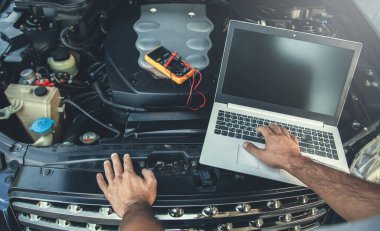 man to repair car with hand computer