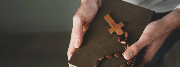 man hand holding cross on Bible on dark background