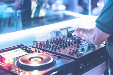 DJ, gece kulübündeki tekno partisinde parlak mavi sahne ışıklarıyla müzik çalıyor. Konserde müzik parçalarını karıştıran profesyonel disk jokeyi. Dj el ses düzeyi düğmesini ayarlıyor.