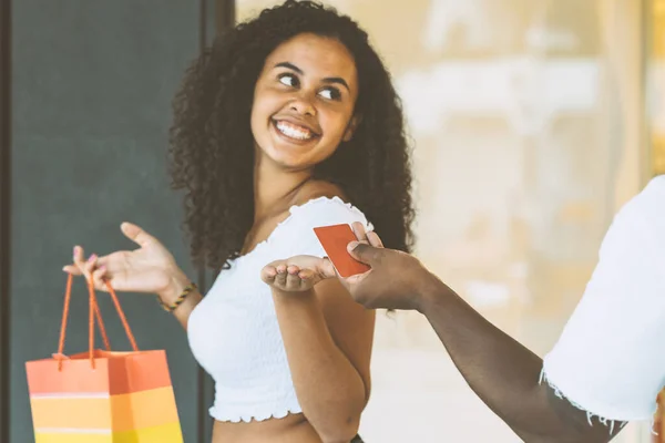 带着信用卡和购物袋的年轻的非洲女孩 购物旺季假期的概念 妇女白天在商场的室外区域 图库图片