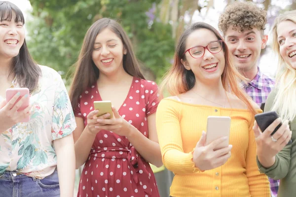 快乐的朋友用智能手机 年轻的学生在玩科技 友谊和大学观念 图库照片