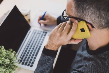 Telefonda konuşurken dizüstü bilgisayarıyla çalışan bir adamın görüntüsü. Kavramsal iş, teknoloji