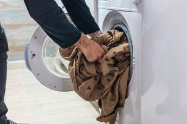 Çamaşırları yıkayan tanınmayan biri. Erkek eli, çamaşır makinesine çarşaf koyuyor.