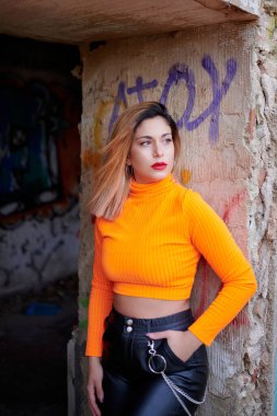 Terk edilmiş bir binada üzerinde duvar yazısı olan parlak bir üst giyen beyaz bir kadının dikey görüntüsü.