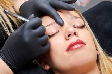 Profesyonel bir makyajcı tarafından kaşlarının düzeltildiği bir kadın fotoğrafı.