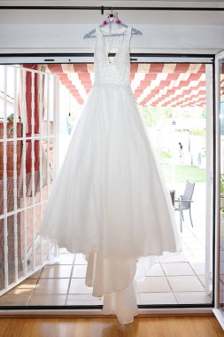 Odada asılı duran beyaz gelinliğin dikey görüntüsü.