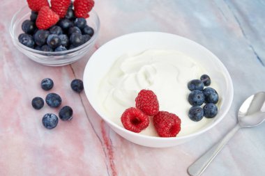 İçinde Yunan yoğurdu, fındık, tahıl gevreği, yabanmersini ve mermer arka planda taze ahududu var.