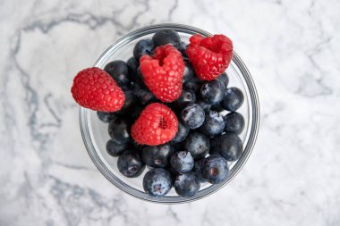 Mermer zemin üzerinde yabanmersini ve taze ahududu olan bir kase. en üstteki görünüm