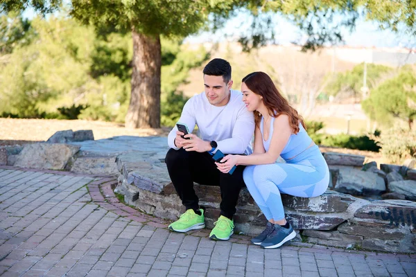 Parkta oturmuş akıllı telefondan online içeriği izleyen genç bir çift.