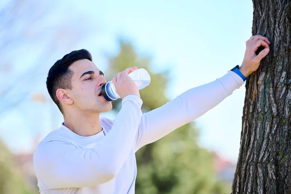 Spor giyimli güzel Avrupalı genç adam eğitimden sonra su içiyor.