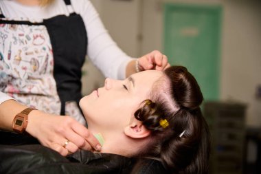 Kuaför makyaj yapıyor ve bir güzellik salonunda genç bir bayan müşteriyi şekillendiriyor.