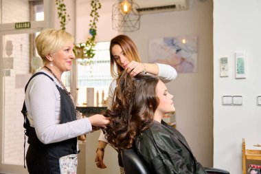 Kuaför makyaj yapıyor ve bir güzellik salonunda genç bir bayan müşteriyi şekillendiriyor.