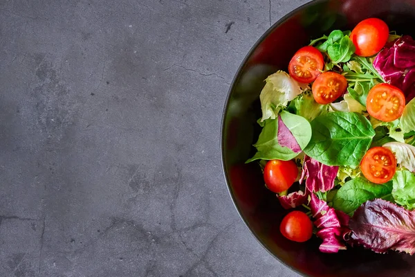 Bir salata marul, domates, kuzu salatası ve siyah bir tabakta salata.