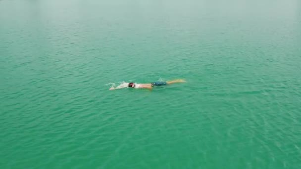 プロの水泳選手がオープンウォーターで泳ぐ 若い男は海で泳いで 美しい紺碧の水 川でプロの水泳選手の空中ビュー 夏には湖でスポーツマンが泳ぐ — ストック動画