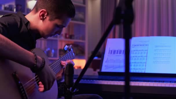 10代の若者の映像が彼の部屋でギターを演奏する 若い男が楽器を演奏する ミュージシャンはプロのマイクを使用して音楽スタジオで彼の作曲を記録します プロの照明 — ストック動画