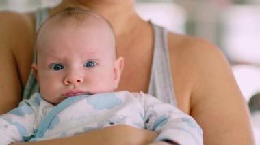 Yeni doğmuş bebek annesinin kollarında. Anne bebeği kollarında tutuyor. Çocuk kameraya bakıyor. Mavi gözlü bir bebek. Yavaş çekim videosu