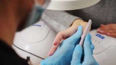 Manikürcü tırnakların şeklini özel bir tırnak törpüsüyle dosyalar, görüntüyü kapat. Manikürcü tırnak törpüsüyle tırnakları şekillendiriyor. Güzellik salonunda tırnak bakımı. Çivi dosyası işleme.