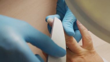 Manikürcü tırnakların şeklini özel bir tırnak törpüsüyle dosyalar, görüntüyü kapat. Manikürcü tırnak törpüsüyle tırnakları şekillendiriyor. Güzellik salonunda tırnak bakımı. Çivi dosyası işleme.