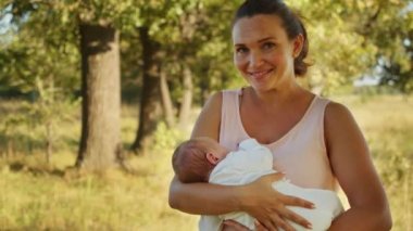 Mutlu anne kucağında bir bebek tutuyor. Açık havada. Sevimli bebek annesinin kollarında uyuyor, yaz, park. Mutlu ebeveynlik kavramı. Anne yeni doğan oğlunu kollarında sallıyor. Anne ve çocuk..