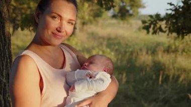 Mutlu anne kucağında bir bebek tutuyor. Açık havada. Sevimli bebek annesinin kollarında, yaz, park. Mutlu ebeveynlik ve annelik kavramı. Anne ve yeni doğmuş oğlu kollarında. Anne ve çocuk..