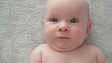 Yeni doğmuş güzel bir bebek. Çıplak göbekli, iki aylık tatlı bir bebek kameraya bakıyor, ağır çekimde. Aktif yeni doğan çocuk yatağa uzanıyor ve kollarını hareket ettiriyor. Tombul bir bebeğin yüksek açılı görüntüsü.