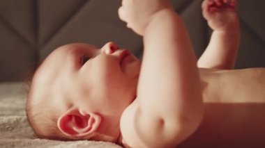 Aktif yeni doğan bebek parmaklarını emiyor, yakın plan, profil görüntüsü. Çıplak göbekli şirin bir bebek yukarı bakıyor, ağır çekimde. Yeni doğan çocuk yatağa uzanıp kollarını hareket ettiriyor. Tombul erkek bebek..