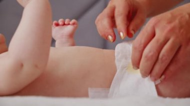 Anne yeni doğmuş bebeğinin altını değiştiriyor. Anne içeride yeni doğmuş bebeğinin altını değiştiriyor. Çocuk bacaklarını oynatıyor. Kuru cilt. Annem yeni doğmuş bebeğinin bezini bir masanın üstüne koyar..