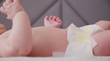 Mutlu yeni doğmuş güzel bebek, yakın çekim yüzü. Çıplak göbekli şirin bir bebek yukarı bakıyor, ağır çekimde. Aktif yeni doğan çocuk yatağa uzanıyor ve kollarını hareket ettiriyor. Tombul bir bebeğin düşük açılı görüntüsü.