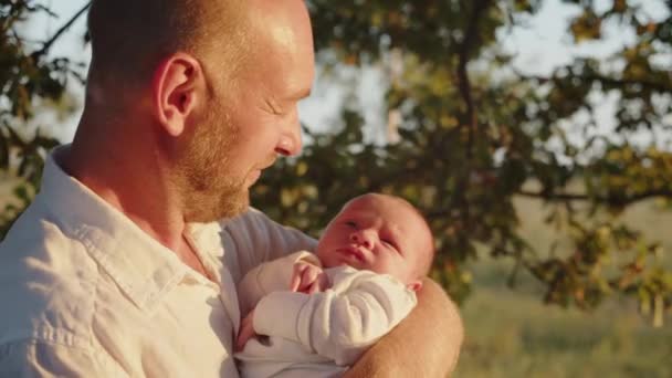快乐的微笑的爸爸正在看着她的新生婴儿 婴儿在父亲怀里 日落时在户外 父亲和新生儿子 父母和孩子 快乐父母的概念 — 图库视频影像