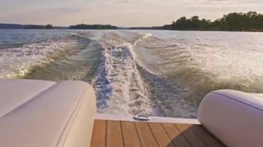 Motorlu tekne çok güzel dalgalar yaratıyor, yüksek hızda hareket eden motorlardan fışkırıyor. Güzel bir yaz günbatımında teknenin kıç tarafından görünüm. 