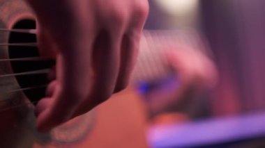 Gitar çalan bir adamın ellerinin yakın çekimi. Müzisyen akustik gitar çalıyor, yakın çekim. Erkek parmaklar gitarda hızlı çalar. İnsan eli gitar ensesinde oynar, yumuşak odaklanır.