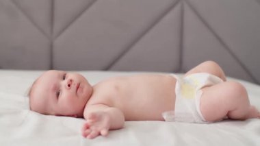 Aktif bebek emme parmakları, profil görüntüsü. Tam vücut. Yeni doğan çocuk yatağa uzanıp kollarını hareket ettiriyor. Tombul erkek bebek. Yavaş çekim.