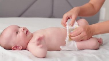 Anne yeni doğmuş bebeğinin altını değiştiriyor. Anne içeride yeni doğmuş bebeğinin altını değiştiriyor. Çocuk bacaklarını oynatıyor. Kuru cilt. Annem yeni doğmuş bebeğinin bezini bir masanın üstüne koyar..