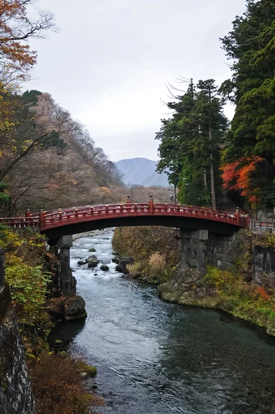 Antiguo puente de arco rojo japonés cruzando arroyo rodeado de Aut — Foto de Stock