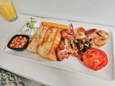 Traditional English Big Breakfast with poached egg, sausage, bacon, tomatos, hash brown, mushroom, and baked beans