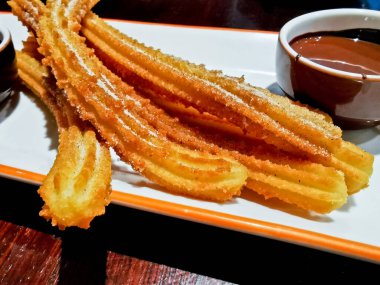 Koyu çikolata soslu kızarmış Tarçınlı Churros beyaz tabakta servis ediliyor.