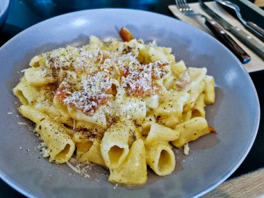 Penne pasta carbonara on white sauce with bacon and extra topping cheese served on blue plate