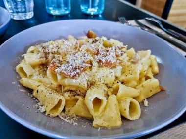 Penne pasta carbonara on white sauce with bacon and extra topping cheese served on blue plate