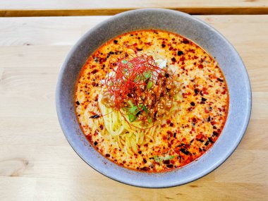 Baharatlı, kırmızı kıymalı, bronzlaşmış, Japon erişteli erişte çorbası sıcak servis edilir.