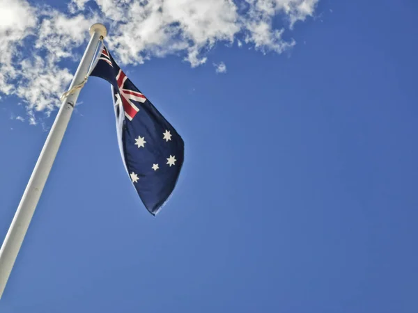 National flag of Australia consists of Union Jack and Southern Cross stars constellation in blue sky sunny day with white cloud