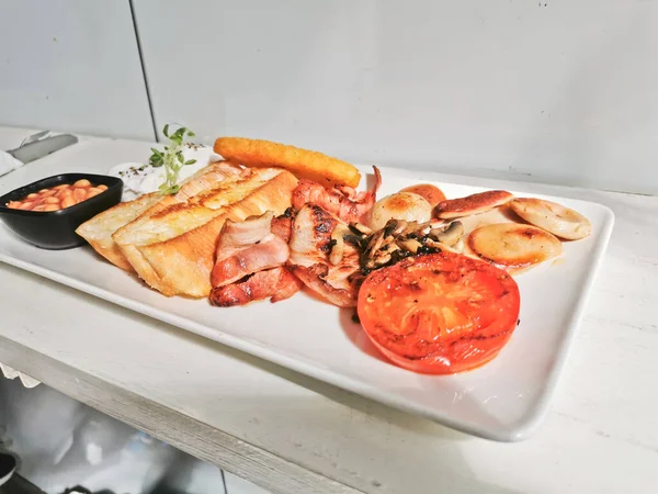 Traditional English Big Breakfast with poached egg, sausage, bacon, tomatos, hash brown, mushroom, and sourdough bread