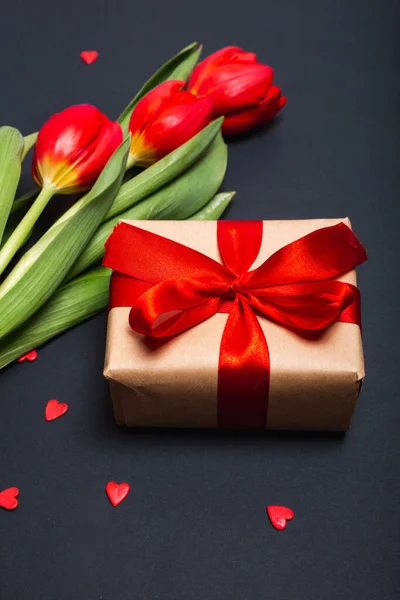 Scatola regalo artigianale con nastro rosso, fiori e cuori di carta su sfondo nero per San Valentino. Festa della mamma. — Foto Stock