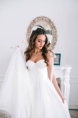 Gelinlikli göz kamaştırıcı gelin stüdyoda dikiliyor ve aşağıya bakıyor.
