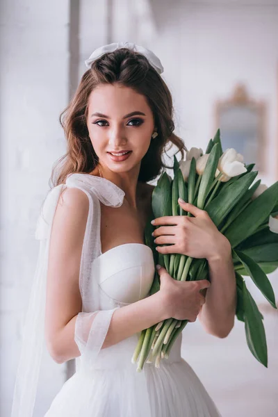Szczęśliwa piękna panna młoda trzyma ślubny bukiet białych tulipanów w jej rękach w studio. — Zdjęcie stockowe