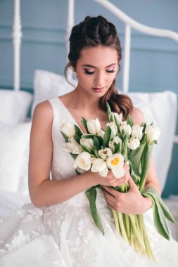 Güzel bir gelin ve bir düğün buketi stüdyodaki gibi kapalı bir odada oturuyor..