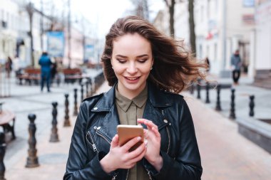 Kaldırımda gezinen ve akıllı telefondan mesaj okuyan odaklanmış bir kadın.