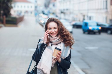 Kahve içen genç bir kadın şehir dışında cep telefonuyla konuşuyor.