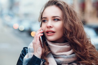 Kahve içen genç bir kadın şehir dışında cep telefonuyla konuşuyor.