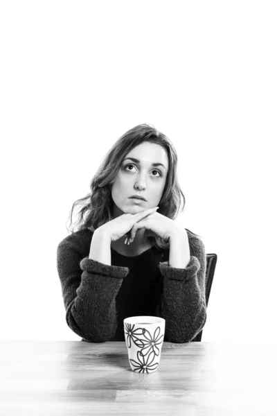 Young woman sitting at table with a cup of coffee looking up. — Stock Photo, Image