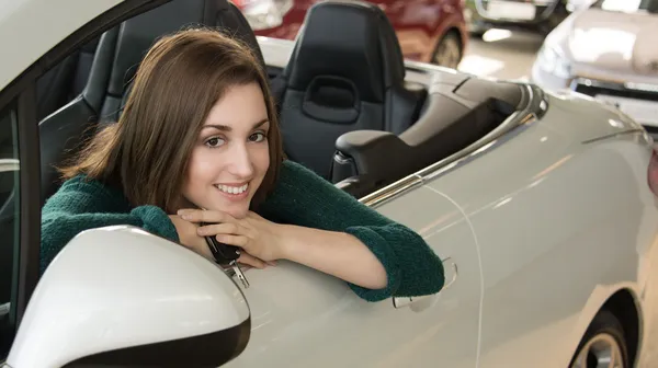 Young brunette holding car key inside car dealership — Stock Photo, Image